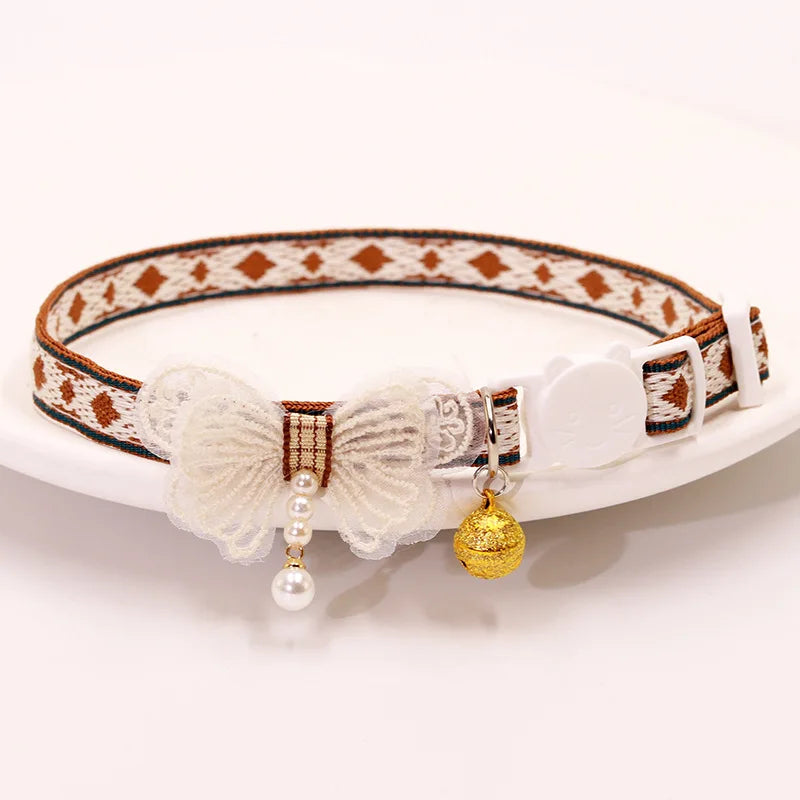 A white leather breakaway cat collar featuring a patterned strap, a bowknot, and a gold bell.