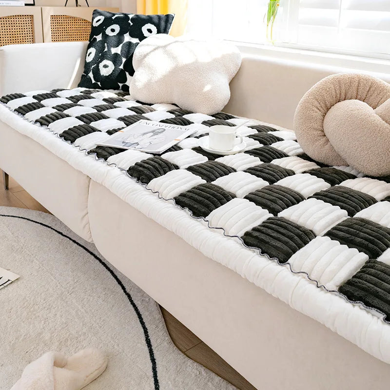 A cozy plush fleece pet bed mat with a black and white checkered pattern is placed on a light-colored sofa.