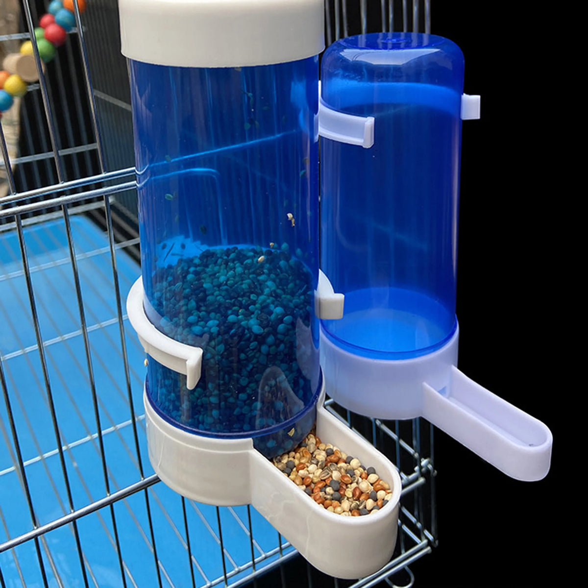 Klares Plastik-Vogel-Wasser- und Futtermittelspender mit blauem Flüssigkeit und einer Ansammlung kleiner Samen im unteren Beh
