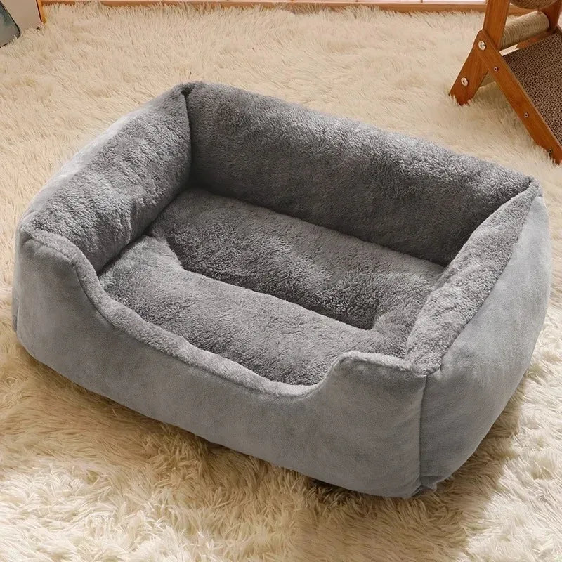 Un coussin de lit pour chat gris en peluche posé sur un tapis blanc moelleux.
