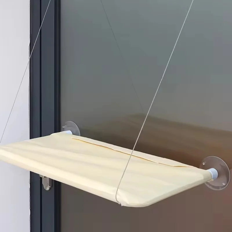 Un lit hamac beige suspendu par de fins cordes d'un cadre de fenêtre.