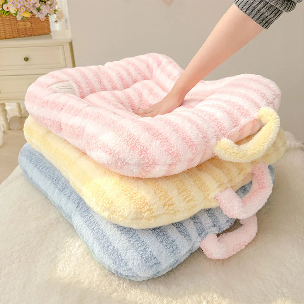 A stack of three plush oval pet beds in pink, yellow, and blue fabric resting on a white surface.