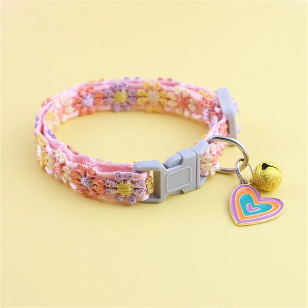 A pink and yellow rainbow flower cat collar with a heart-shaped bell attached.