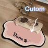 A pet feeding mat featuring a cute cat and a Dana brand name, holding seeds in bowls.