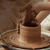 A hand is dipping a piece of natural clay into a ceramic pot for aquarium decoration.
