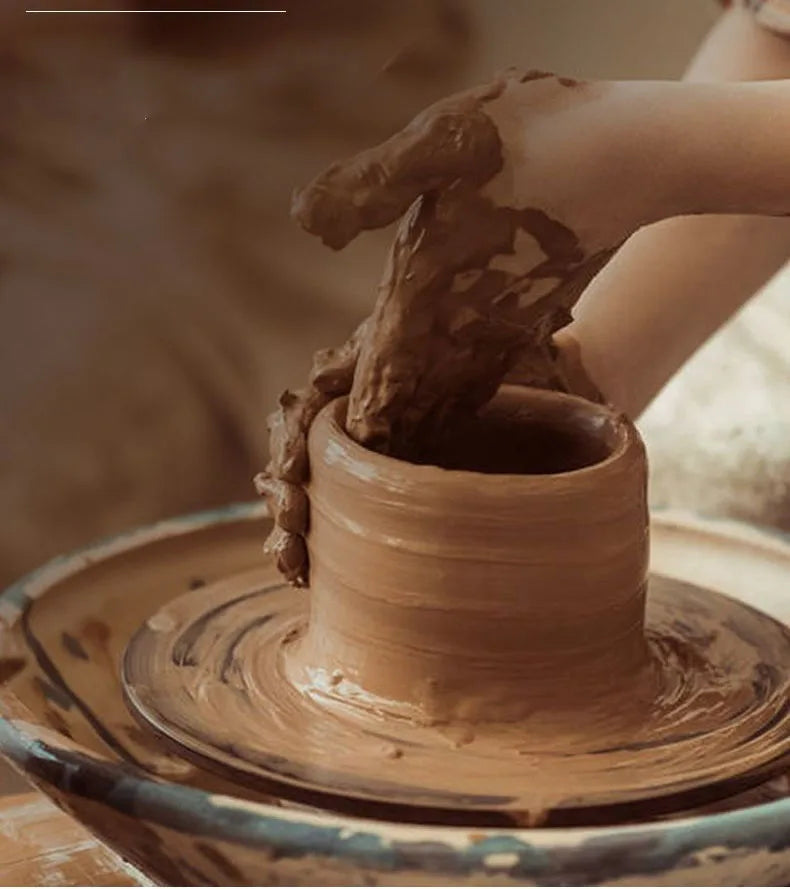A hand is dipping a piece of natural clay into a ceramic pot for aquarium decoration.