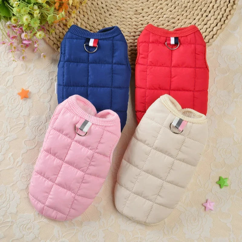 Trois manteaux imperméables en duvet pour chien, bleu marine, rouge et beige, posés sur un fond clair.
