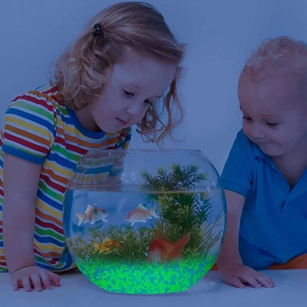 A young girl is looking into a glass bowl filled with glowing green water and aquatic plants.