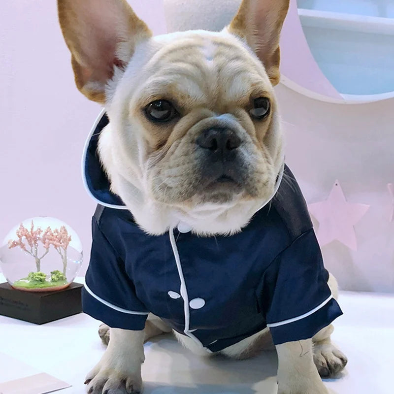 A fawn-colored dog wearing a dark blue silk pajama top with white trim.