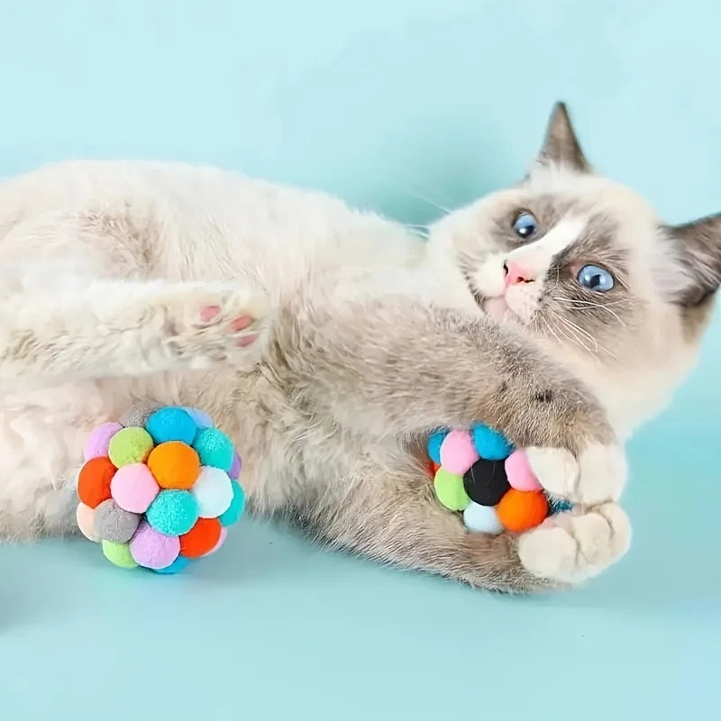 A small kitten is interacting with colorful, soft jingle bell-shaped cat toys.