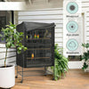A black bird cage cover with a wire mesh interior is displayed on a wooden deck next to potted plants.