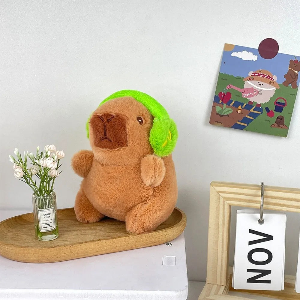 Brauner Capybara-Plüschtier mit leuchtendgrüner Kapuze neben einer gerahmten Illustration.