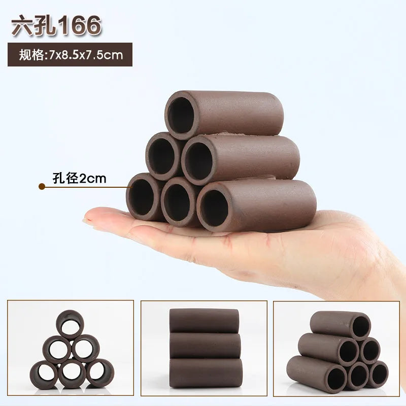 A hand holds several cylindrical natural clay aquarium cave decorations for fish and shrimp.