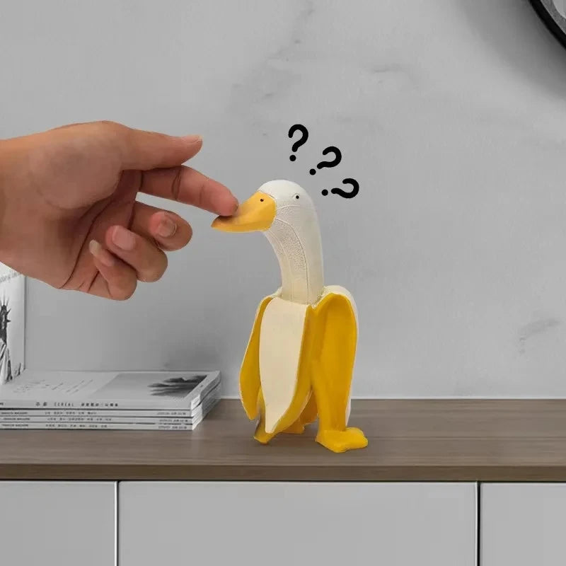 Eine gelb-weiße Bananenduck-Gartenskulptur neben einer Hand mit Fragezeichen auf einer Holzoberfläche.