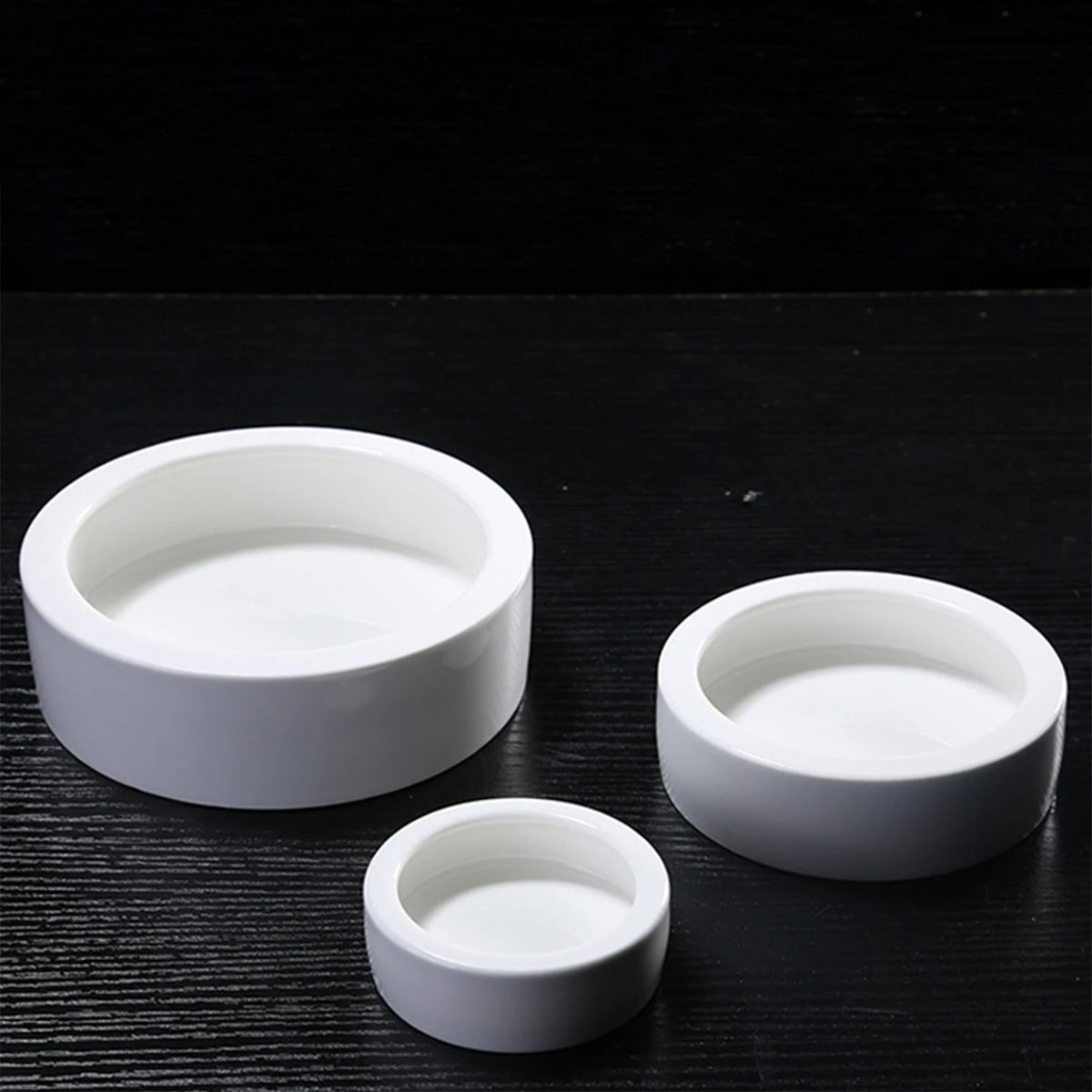 A set of three white ceramic reptile feeding bowls placed on a dark surface.
