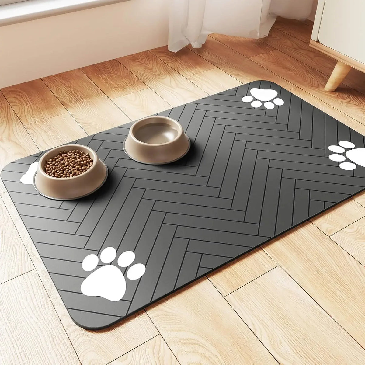 A gray pet feeding mat with a herringbone pattern on a wooden floor, featuring paw print designs and a ceramic bowl.