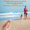A hand holds a small, orange ultrasonic dog bark deterrent device on a sandy beach with the ocean in the background.