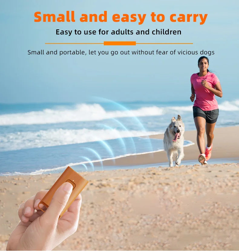 A hand holds a small, orange ultrasonic dog bark deterrent device on a sandy beach with the ocean in the background.