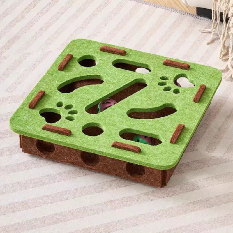 A green felt maze puzzle toy for cats with holes and a bell ball is shown on a striped surface.