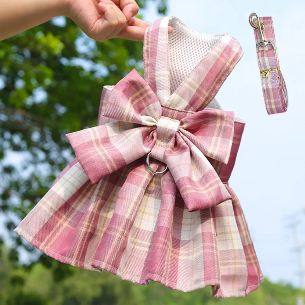 A pink plaid dress for a dog with a bow and a matching harness clip.
