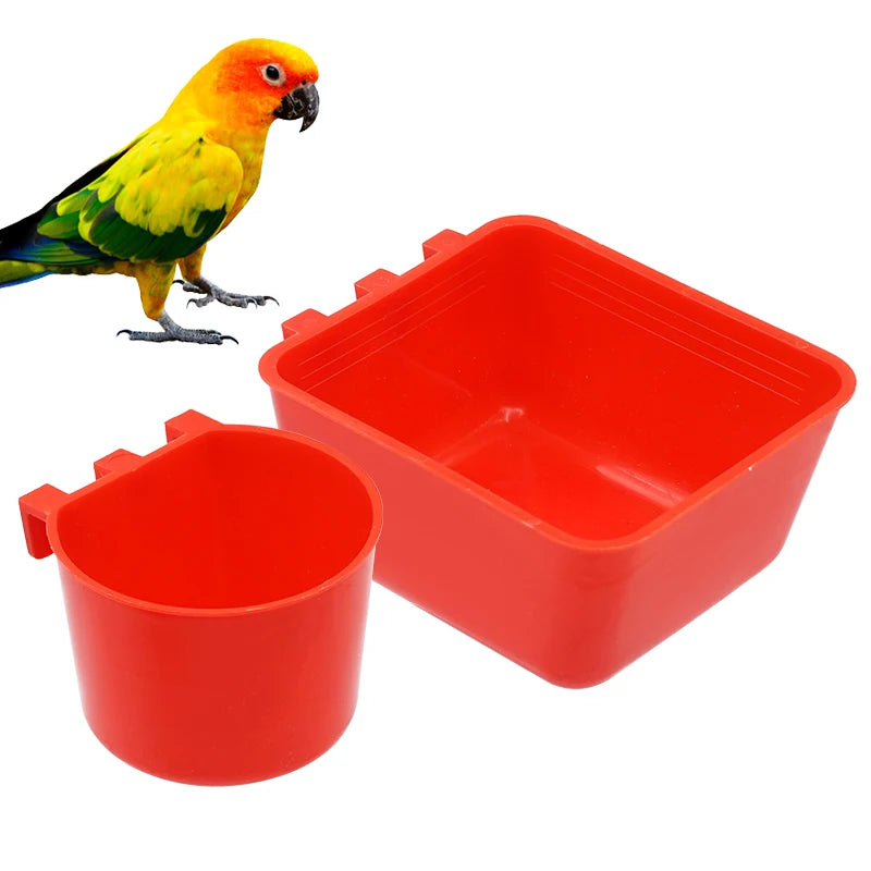 A bright yellow and green parrot perched next to a red plastic bird feeder and water bowl.
