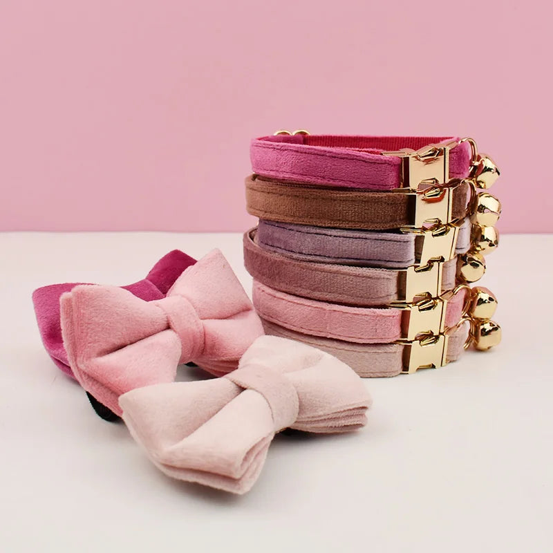 A stack of pink and mauve velvet cat collars with gold hardware displayed on a white surface.