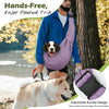 A man wearing a blue hoodie is carrying a dog in a purple hands-free sling carrier outdoors.