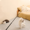A fluffy white cat is playing with an extended telescopic wand toy on a light-colored carpet.