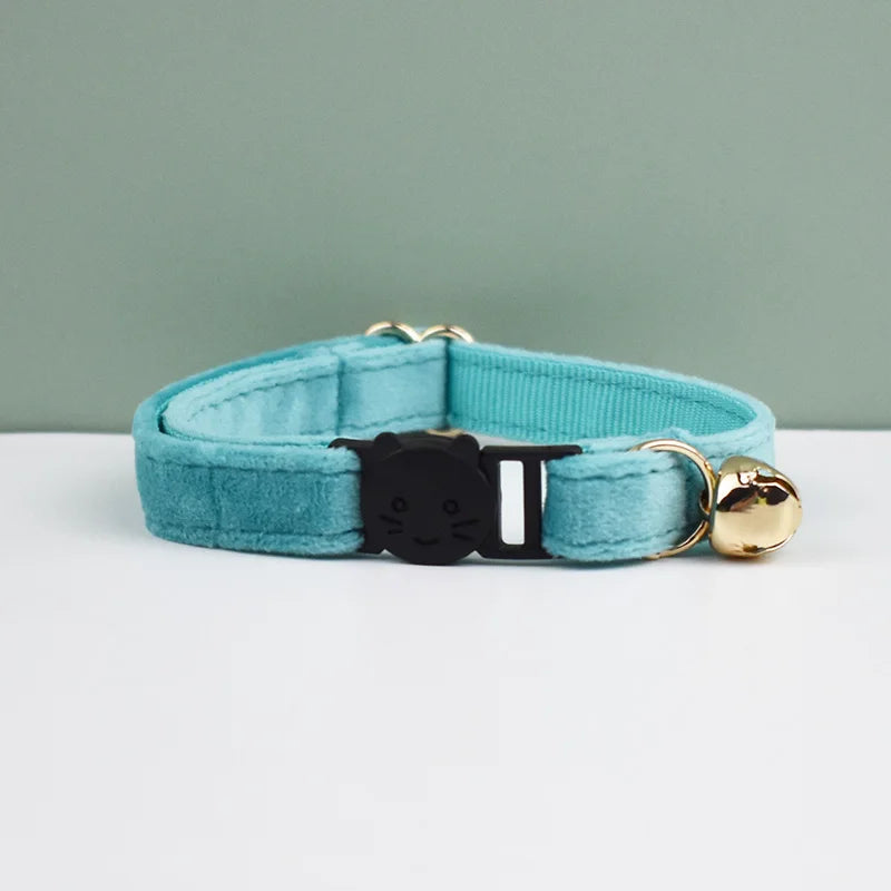 A teal velvet cat collar with a black cat charm and gold hardware, displayed on a white surface.