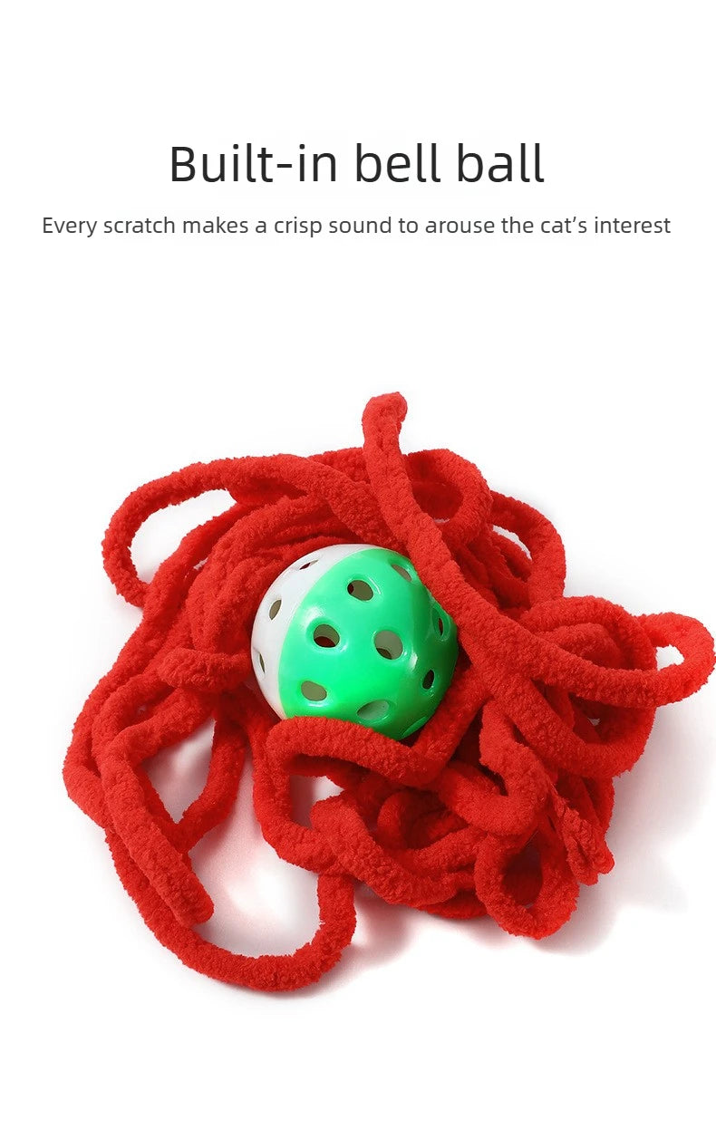 A bright red yarn ball with a green bell is tangled, ready for a cat toy.