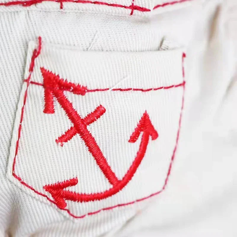 A close-up of a white fabric garment showing a red embroidered anchor patch on the pocket.