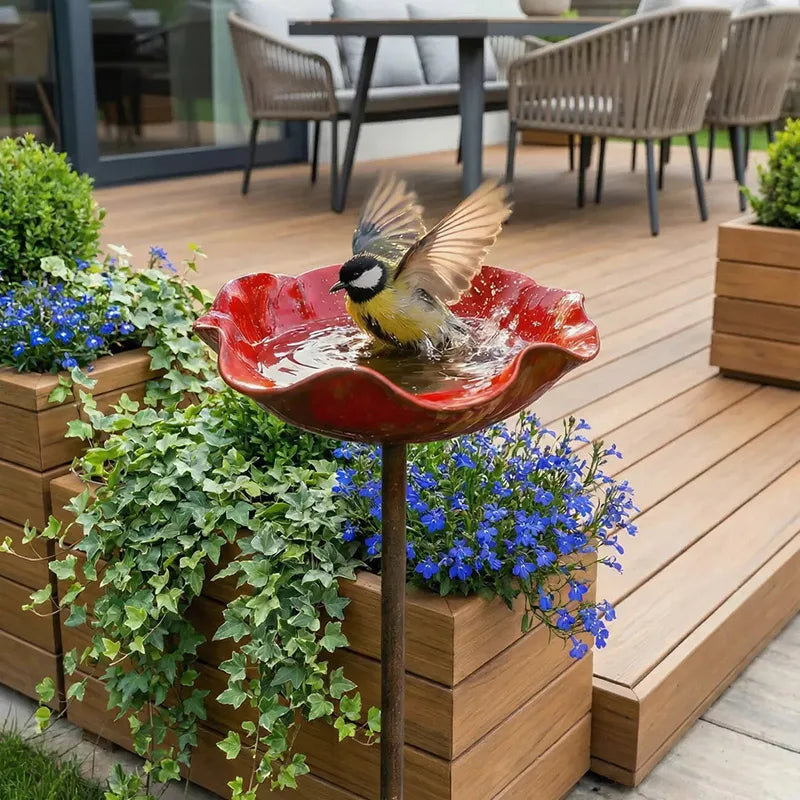 A small, flower-shaped outdoor bird bath with a red bowl is filled with water and features a plug-in installation.