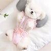 A fluffy white dog wearing pink shorts lying on a white surface.