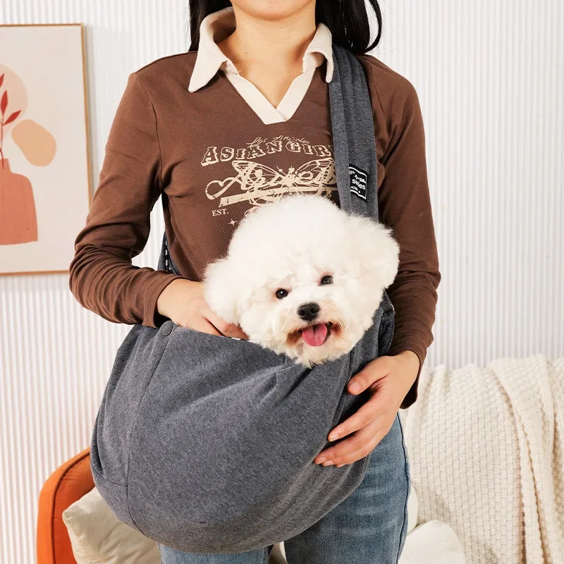 Eine Person hält einen weißen flauschigen Hund in einem grauen, leichten Pet-Crossbody-Sling-Tragegurt.