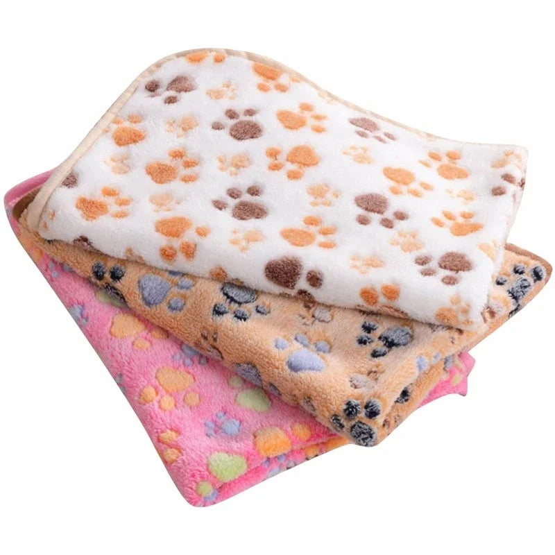 A stack of cozy flannel fleece pet blankets featuring various paw print designs in orange, gray, and pink.