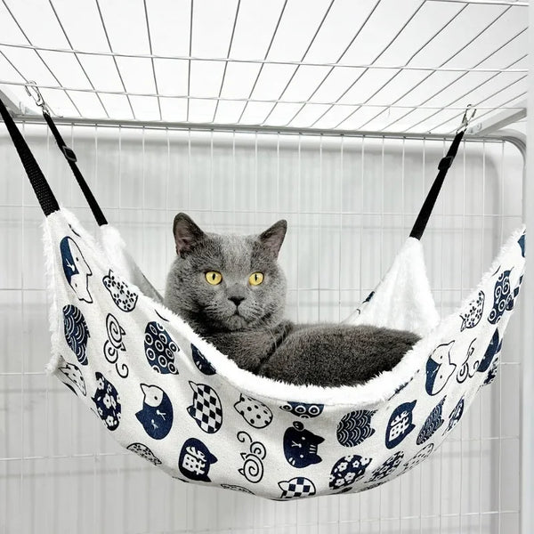 A gray cat is relaxing in a white and blue patterned pet hammock sleeping bag suspended by a wire grid.