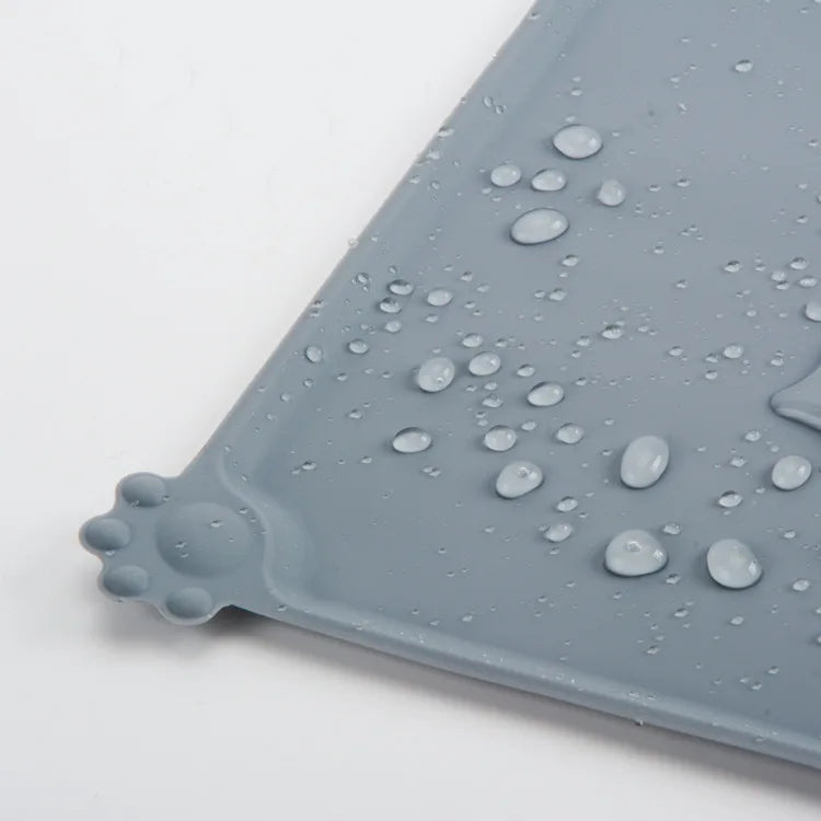 A gray silicone pet feeding mat with raised edges and water droplets on its surface.