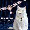 A white cat wearing a pearl and gemstone necklace against a dark blue background.