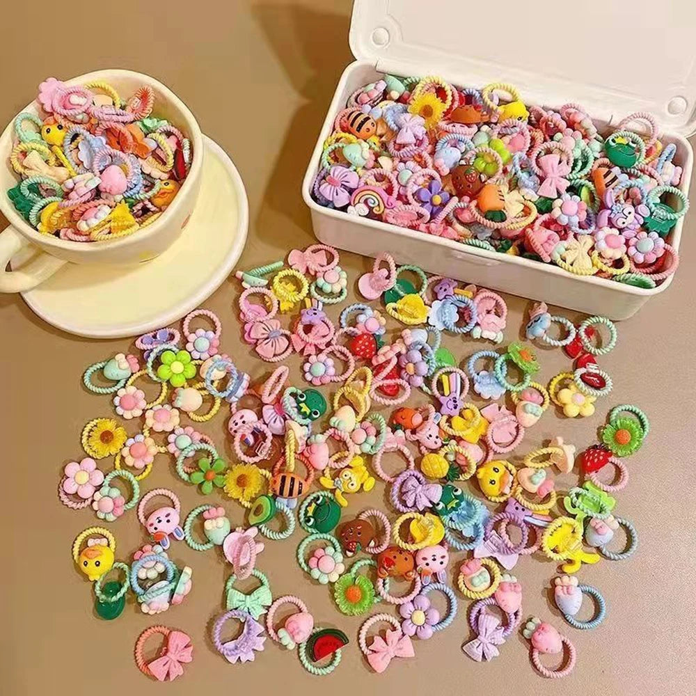 A variety of colorful elastic hair ties and accessories for kids are displayed in a white box and scattered on a surface.