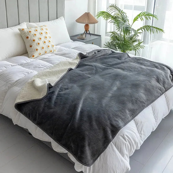 A dark gray waterproof pet blanket is draped over a white duvet on a bed.