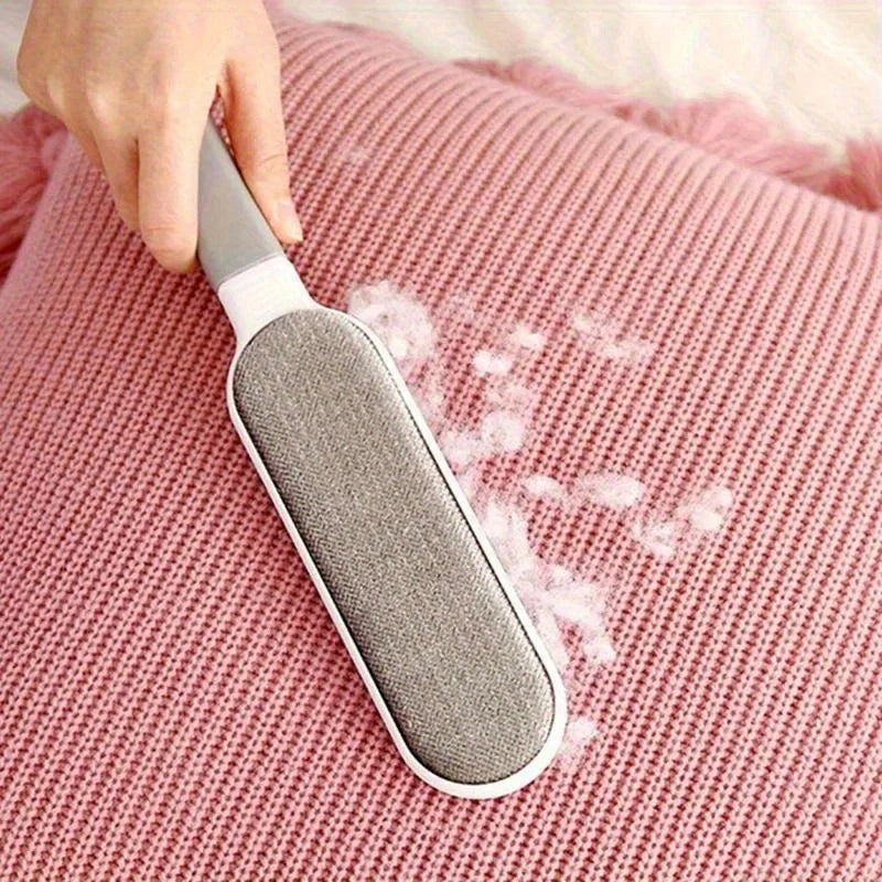 Une main tient une brosse retire-poils grise et blanche sur une surface texturée rose.