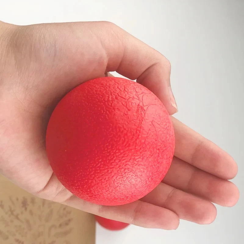 A hand holds a bright red rubber dog ball against a light background.