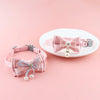 Pink lace bow cat collar with a pearl bell and bead charm displayed on a white plate.