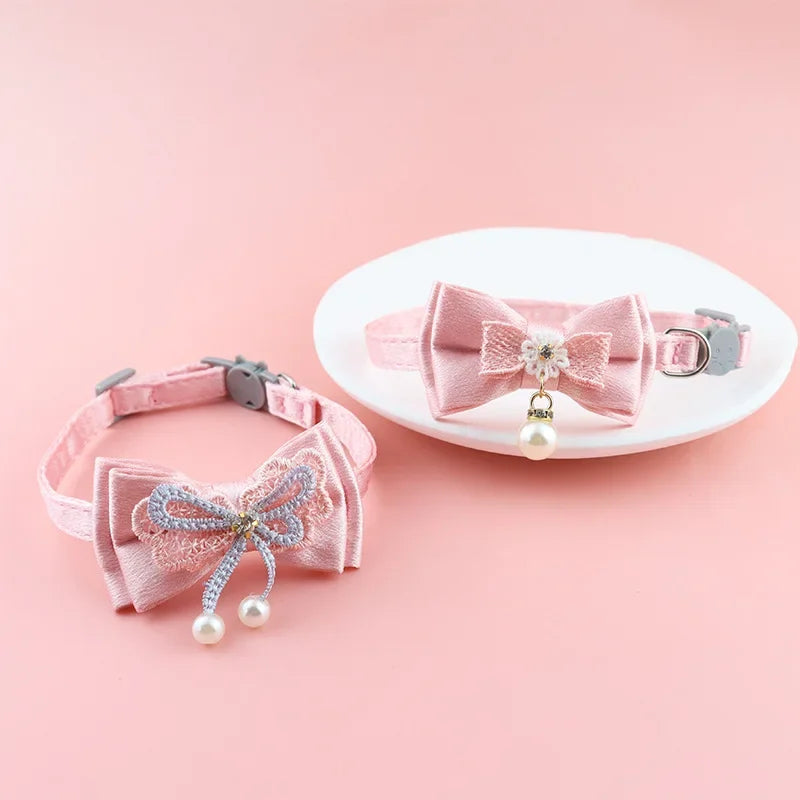 Pink lace bow cat collar with a pearl bell and bead charm displayed on a white plate.