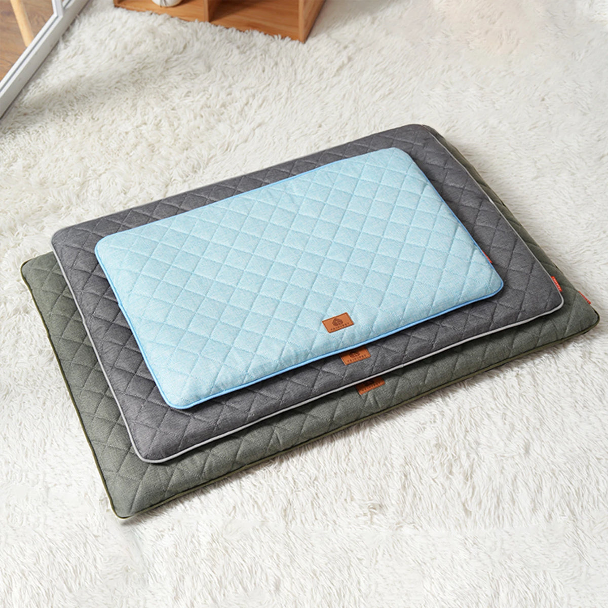 A light blue quilted washable dog sleeping mat is placed on a gray protective mat on a white fluffy rug.