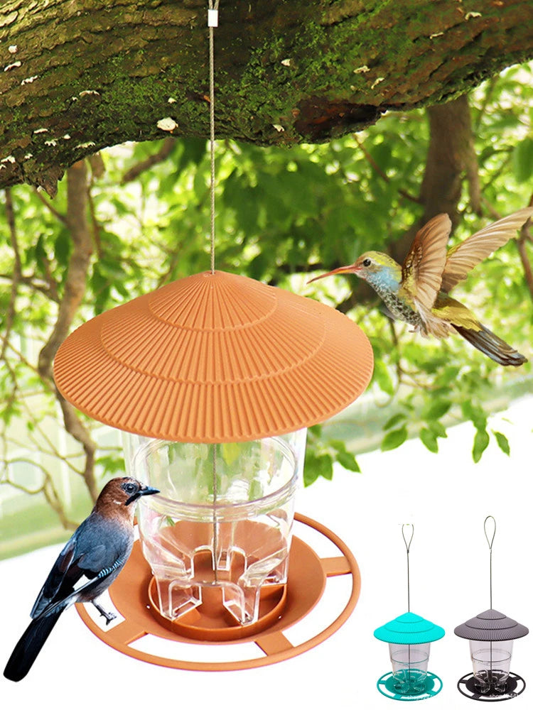 Nourriceur à graines pour oiseaux orange et imperméable avec bol en verre et base métallique, suspendu à une branche d'arbre.