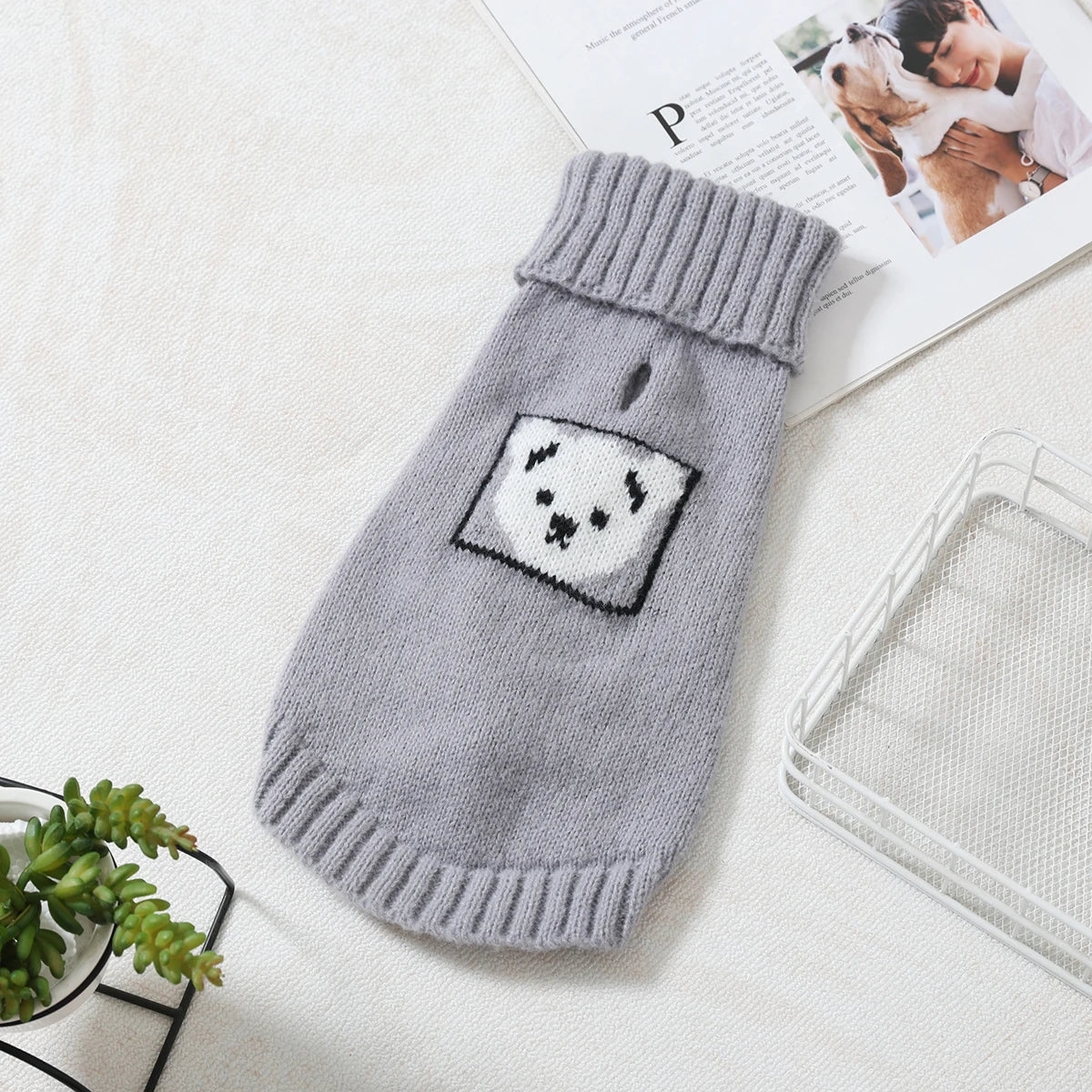 A gray knitted pet sweater with a white panda face design lying on a white surface.