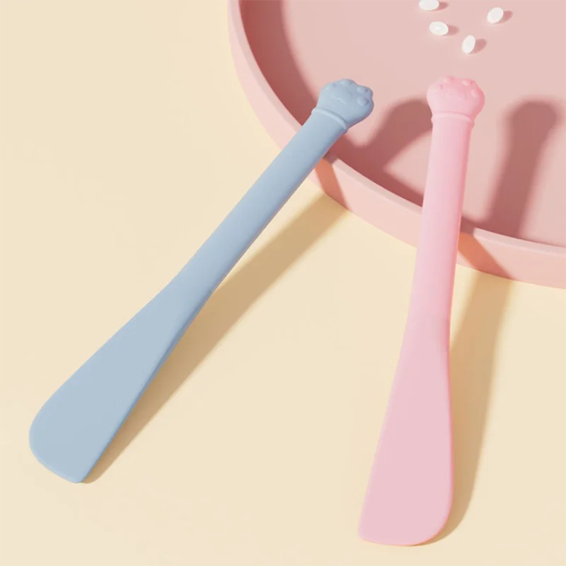 A light blue pet feeding spoon and a pink pet feeding spoon are shown on a pink plate.