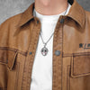 A close-up of a brown leather jacket featuring a Jason Mask pendant necklace on a white shirt.