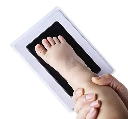 Un kit d'empreinte de main et de pied montrant le pied d'un bébé pressé dans un cadre blanc par la main d'un adulte.